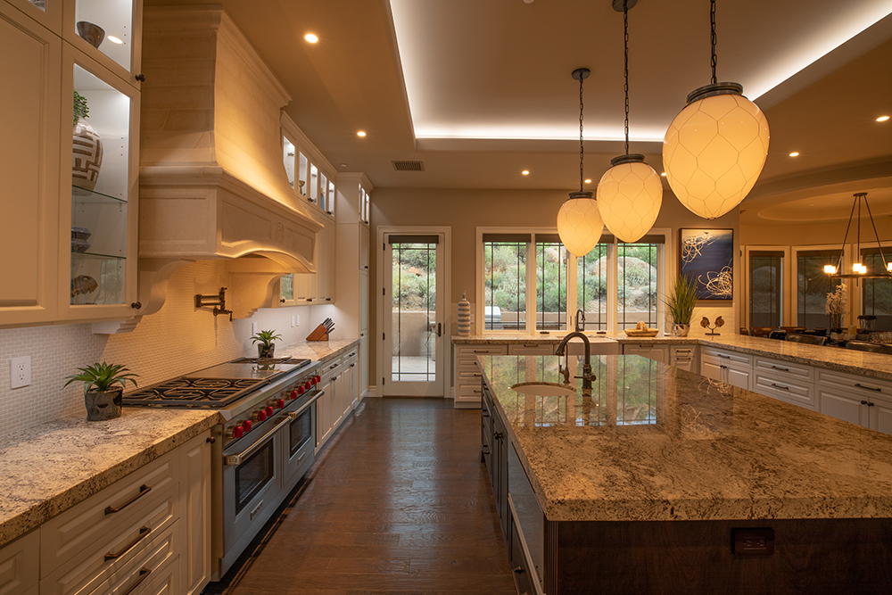 A kitchen with a lighting scene activated. There are can lights, pendants, under cabinet and cove lights in the image. One of the benefits of a lighting control system is the ease of activating a scene.
